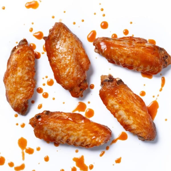 Five Zee's Kitchen American chicken wings, coated in orange sauce, scattered on a white surface.
