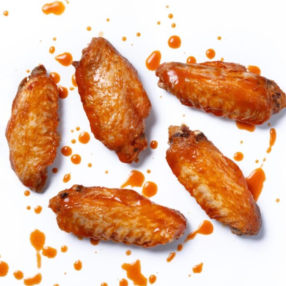 Five Zee's Kitchen American chicken wings, coated in orange sauce, scattered on a white surface.