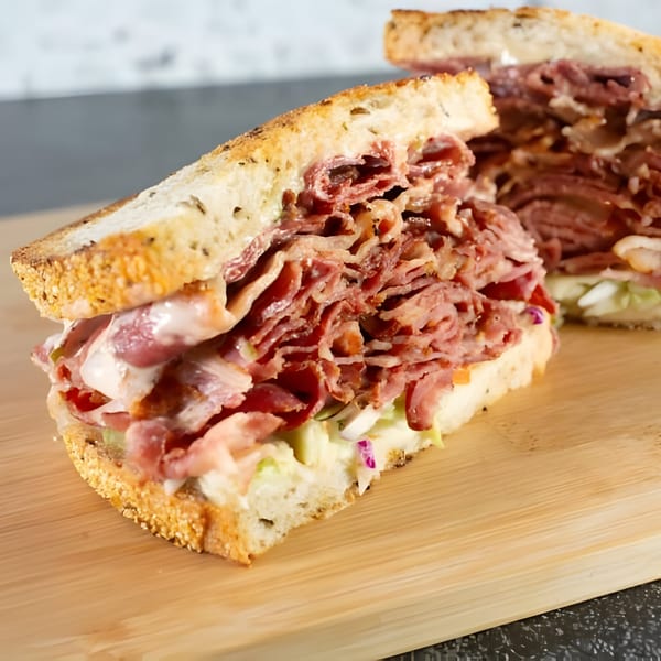 Two halves of a hearty Zee's Kitchen pastrami sandwich with coleslaw on toasted bread.