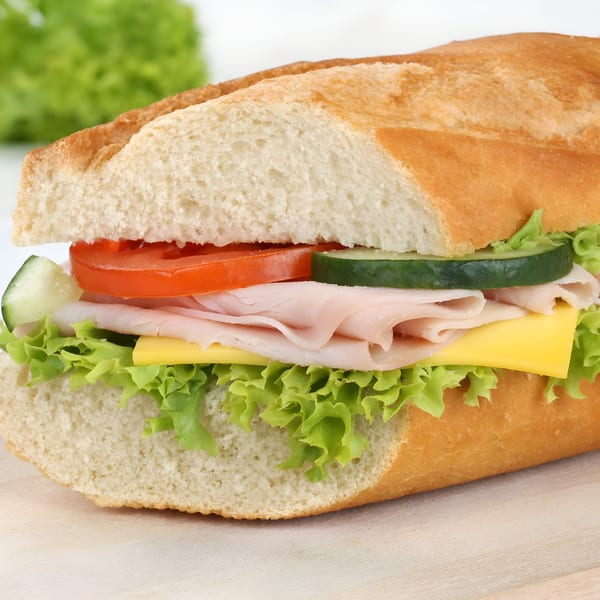 Close-up of a Zee's Kitchen baguette sandwich with turkey, cheese, lettuce, tomato, and cucumber.