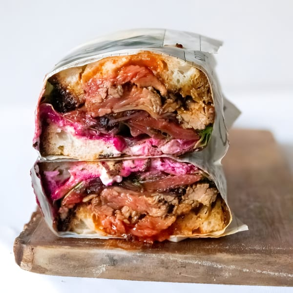 A large American sandwich, cut in half, revealing layers of meat, pink sauce, and vegetables.