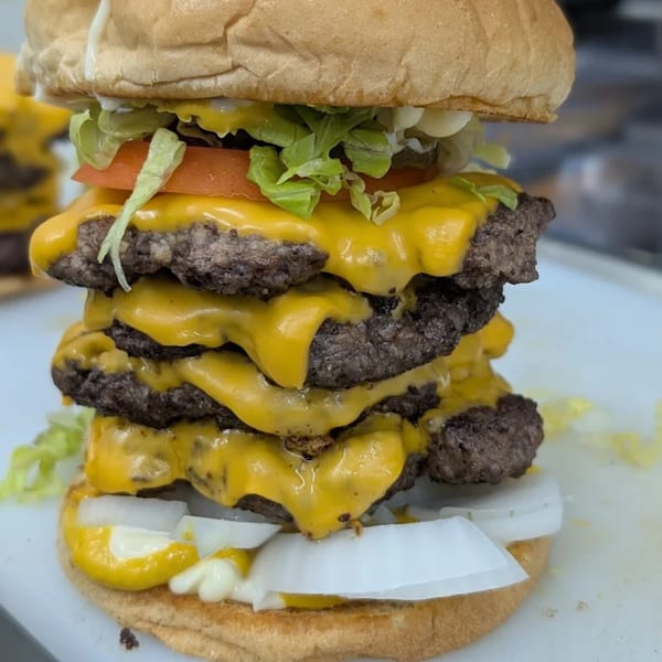 A towering quadruple cheeseburger from Zee's Kitchen, with melted cheese, lettuce, tomato, and onions.