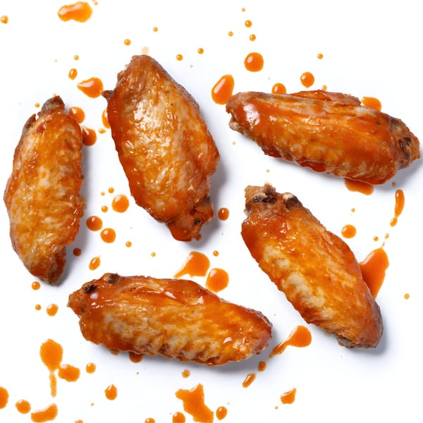 Five Zee's Kitchen American-style chicken wings, coated in orange sauce, scattered on a white surface.